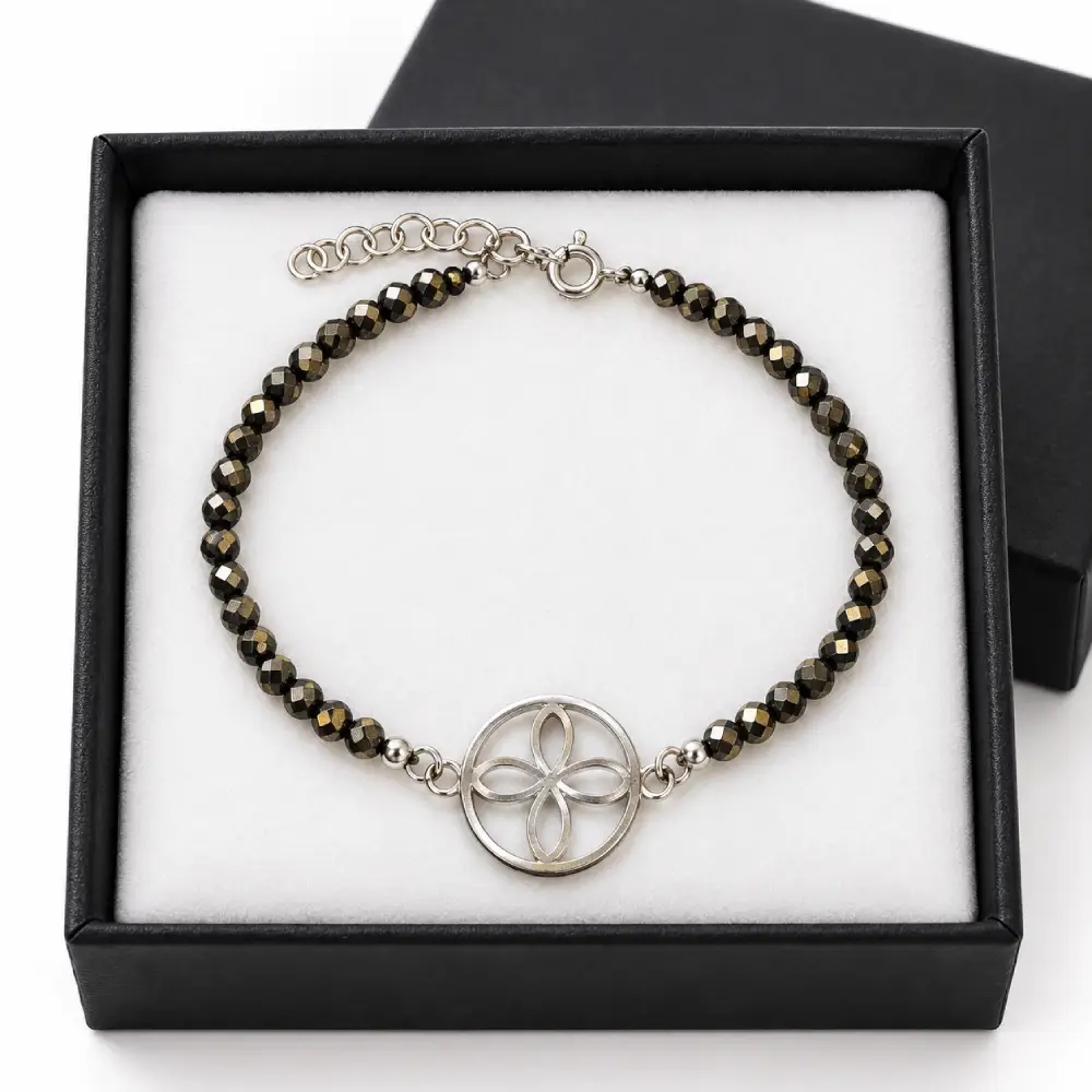 Pulsera Sigilo de la Abundancia con Pirita y Plata de Ley 1 Pulsera de pirita facetada con sigilo circular y cierre de plata de ley sobre almohadilla blanca en caja negra.